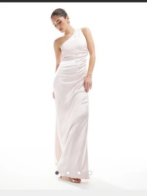 Ljus oneshoulder långklänning - Elegant ljus långklänning med oneshoulder-design och draperad effekt över kroppen. Klänningen har en slank passform och är tillverkad i ett glansigt material som ger en lyxig känsla. Perfekt för balen eller bröllop. Köpte den som förslag till balklänning men valde en annan till slut. Hoppas den kommer till nytta för någon annan. Slutsåld på asos och vet inte om den går att köpa någon annanstans så passa på🥰