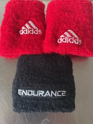 Adidas & Endurance svettband - Två sportiga svettband, ett rött från Adidas med broderad logga och ett svart från Endurance med vit text. Perfekta för träning och sportaktiviteter. Tillverkade i mjukt och absorberande frottématerial.    3 st 