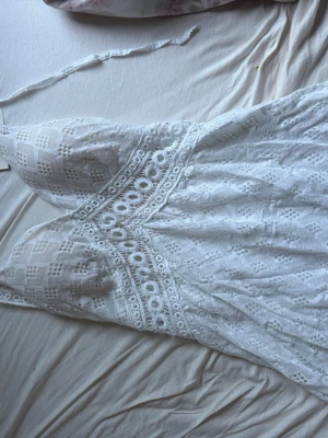 Student (helt ny) Vit spetsklänning med smala axelband - Söt vit kortklänning med smala axelband och v-ringning. Klänningen har fina spetsdetaljer och broderade mönster över hela tyget samt dekorativa hålbroderier i midjan. Perfekt för sommarens alla tillfällen.