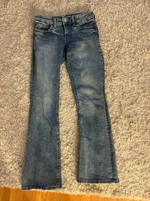 Blå bootcut jeans  - Ett par blå bootcut jeans med klassisk femficksmodell. Jeansen har låg midja och är tillverkade i denim med en snygg tvättad look. Perfekta för dig som gillar en avslappnad men trendig stil.