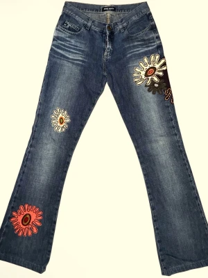 Blå bootcut jeans med broderade mönster - Unika blå bootcut jeans från Miss Sixty med färgglada broderade blommor och grafiska mönster på benen och bakfickan. Jättefina🥰är strl 27 i midjan men passar mig som har 25/26 i midja!🤗