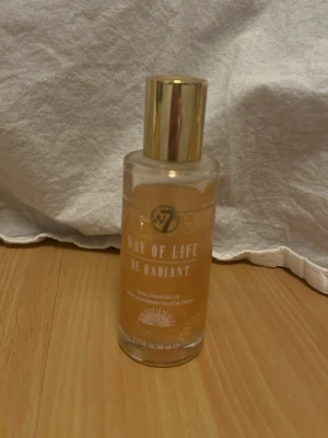 W7 Way of Life Body Shimmer Oil - Glittrande kroppsolja från W7 i nyansen 'Be Radiant'. Oljan kommer i en genomskinlig glasflaska med guldfärgat lock och innehåller massor av guldskimmer som ger huden en snygg glow. Perfekt för att boosta lystern till huden och få en fräsch finish.