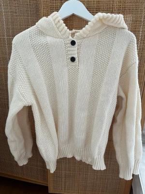 Stickad hoodie i off-white 36/38 - Stickad hoodie i off-white – Perfekt för mysiga dagar! ✨  Denna fantastiska stickade huvtröja i en vacker benvit/off-white nyans.   Oversize/avslappnad passform med nedhasade axlar. En mix av klassisk rätstickning och strukturstickning (moss-stickning).  Mycket fint skick, väl omhändertagen.  Den passar lika bra till ett par jeans som över en klänning eller för en snygg "loungewear"-look hemma. Storlek är okänt men ungefär som 36/38 (S/M)  Kommer från ett rökfritt och djurfritt hem