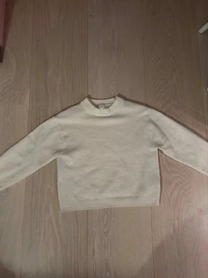 Beige stickad tröja med rund hals - En enkel och stilren beige stickad tröja med rund hals och långa ärmar. Tröjan har ribbade muddar vid ärmslut och nederkant. Perfekt för lager på lager och passar till det mesta i garderoben.