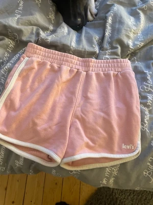 Rosa shorts från Levi's med vit kant - Säljer ett par mjuka rosa shorts från Levi's med vit kant och resår i midjan. Shortsen har en sportig look och är tillverkade i stickat material som känns skönt mot huden. Perfekta för en avslappnad stil.