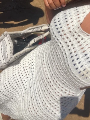Strandklänning - Snygg vit stickad långklänning med hålmönster och ärmlös design. Perfekt för varma dagar och strandhäng. Klänningen har en kroppsnära passform och är tillverkad i ett mjukt stickat material.