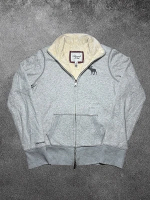 Vintage Abercrombie & Fitch fodrad zip up cardigan - herr strl XL (passar som M) - Säljer en vintage Abercrombie & Fitch fodrad zip up cardigan i ljusgrå färg med broderad logga på vänster sida av bröstkorgen samt Abercrombie broderat nedtill på höger ärm.  👕 Märke: Abercrombie & Fitch 📏 Storlek: XL, passar som M 🎨 Färg: Ljusgrå 🧵 Material: 90% bomull, 10% polyester 📐 Mått: 65 cm lång, 55 cm bred 📌 Skick: Mycket bra skick (se bilder)  💬 Hör av dig vid frågor 💰 Pris kan diskuteras vid snabb affär 📦 Skickas inom 24 timmar