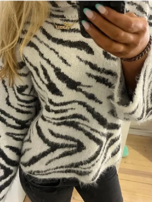 Zebramönstrad stickad tröja från H&M - Säljer en fluffig stickad tröja från H&M med zebramönster i svart och vitt. Tröjan har lång ärm, rund halsringning. Perfekt för dig som gillar djurmönster och vill ha något mjukt och snyggt.