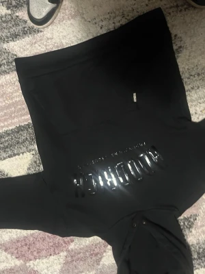 Svart hoodie från Hoodrich XS - Säljer en svart hoodie från Hoodrich i storlek XS. Hoodien har en stor huva, magficka och glansig Hoodrich-logga framtill. Perfekt för dig som gillar streetwear och vill ha en stilren look.