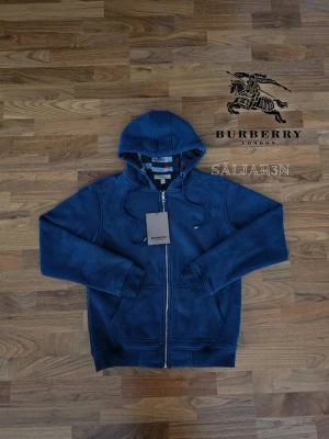 Marinblå Burberry Hoodie  - Letar du efter en stilren och lyxig hoodie? Denna helt nya marinblåa Burberry-hoodie kombinerar elegans med hög komfort. Den har Burberrys ikoniska rutmönster i fodret och en diskret logga på bröstet för en exklusiv touch. Liten i storleken! Tillverkad av mjukt, slitstarkt material och utrustad med dragkedja samt huva – både praktisk och stilfull.  📌 Skick: Ny med taggar. 📦 Snabb leverans🙏