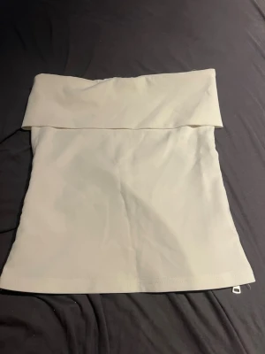 Beige tubtopp med dragkedja - Stilren beige tubtopp med bred kant upptill och en snygg silverfärgad dragkedja på sidan. Toppen har en enkel och clean design, perfekt att matcha med jeans eller kjol. Materialet känns mjukt och stretchigt.