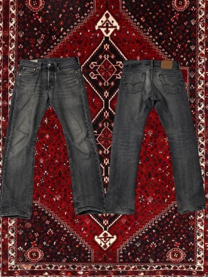 Levi's 501 svarta raka jeans - Säljer ett par klassiska Levi's 501 jeans i svart tvättad denim med raka ben och fem fickor. Jeansen har knappgylf, läderpatch bak och den ikoniska röda Levi's-taggen vid bakfickan. Perfekta för en avslappnad och tidlös stil. W26 och L30