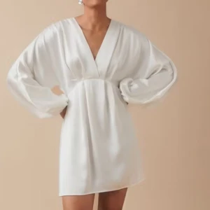 Vit klänning från Gina Tricot - Säljer en elegant vit klänning från Gina Tricot med v-ringning och långa ärmar. Klänningen är tillverkad i ett glansigt material som ger en lyxig känsla. Perfekt för speciella tillfällen!