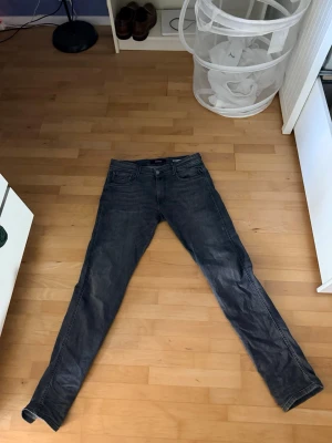 Replay anbass W32 L34 - Säljer ett par mörkgrå slim fit jeans med klassisk femficksdesign och dragkedjegylf. Jeansen har en smal passform och är tillverkade i ett mjukt denimtyg som ger en snygg och modern look.
