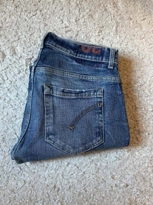 Dondup George Modell - Säljer ett par blå jeans från Dondup med skinny fit och slitna detaljer på både fram- och baksida. Jeansen har klassiska fem fickor och är tillverkade i denim med snygg tvätt och slitningar 