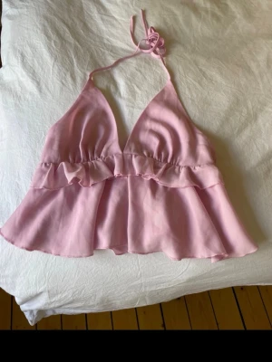 Ljusrosa volang topp med knyt - Supersöt ljusrosa linnetopp med volangdetaljer och knyt i nacken. Toppen har v-ringad form och är ärmlös, perfekt för varma dagar. Tillverkad i ett tunt och luftigt material som känns skönt mot huden. köpte den av någon här på plick så vet tyvärr inte vart den e ifrån❣️