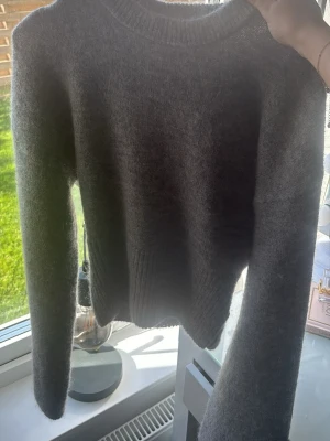 Mörkgrå stickad tröja - Mysig mörkgrå stickad tröja med rund halsringning och långa ärmar. Tröjan har en enkel, klassisk design med ribbstickade muddar vid ärmslut och nederkant. Perfekt för lager på lager och passar till det mesta i garderoben.