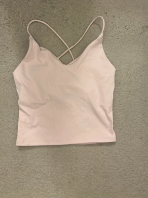 Ljusrosa strappy linnetopp Gina Tricot - Supersöt ljusrosa linnetopp från Gina Tricot med tunna korsade axelband i ryggen. Perfekt för en trendig och avslappnad look. Tillverkad i mjukt syntetmaterial som sitter skönt mot kroppen.
