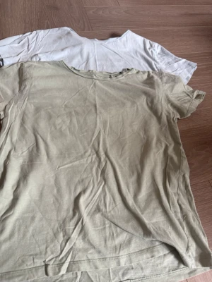 Två basic t-shirts i bomull - Två enkla t-shirts i bomull, en i grön och en i blå. Båda har rund halsringning och korta ärmar. Perfekta för en avslappnad stil och lätta att matcha med andra plagg.