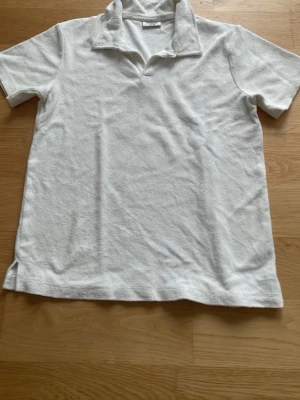 Vit frottépiké med krage - Vit kortärmad pikétröja i mjuk frotté med klassisk krage och v-ringad hals. Perfekt för en avslappnad och trendig look. Enkel och stilren design som passar till mycket.