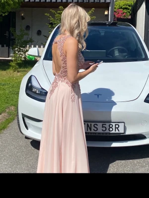 Ljusrosa långklänning med spetsdetaljer - Säljer min super fina ljusrosa balklänning! Endast använd vid ett tillfälle. Klänningen har öppen rygg och vackra detaljer framtill. Den har även som en inlagd BH med ilägg som ger bra stöd. Klänningen är uppsydd efter min längd (164cm) 