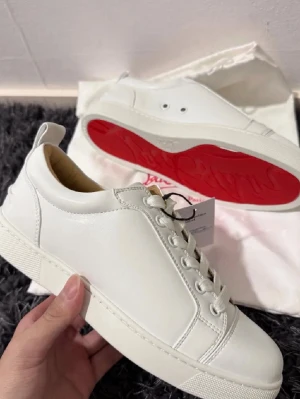 Vita Louboutin sneakers med röd sula - Snygga vita sneakers från Christian Louboutin i läder med den ikoniska röda sulan. Klassisk låg modell med vita skosnören och diskreta detaljer. Perfekta för dig som vill ha en clean look med en lyxig twist.Bilderna är från när jag köpte dom från plick och jag har tröttnat på dom så därför säljs dom, dom är lite smutsigare nu men inte förstörda eller något liknande går att tvätta fint. (unisex) storleken är lite större än 38 skulle jag sagt har själv 38 och dom är lite större (PRIS KAN DISKUTERA