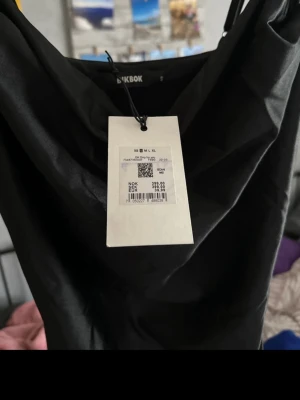 Svart satin klänning från Bik Bok - Snygg svart klänning från Bik Bok i glansigt satinmaterial. Klänningen har tunna axelband och en draperad urringning som ger en elegant look. Perfekt för dig som vill ha en stilren och trendig outfit.