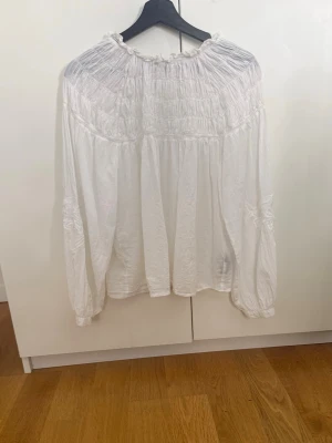 Vit  blus med rynkad hals - Säljer en vit blus med rynkad halsringning och långa, luftiga ärmar. Blusen har en lös passform och fina detaljer vid axlar och ärmslut. Perfekt för en avslappnad och trendig look.