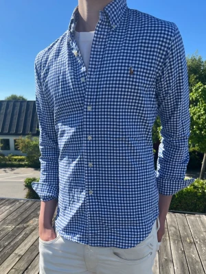 Blårutig skjorta från Ralph Lauren - a(Moddelen är 185 och väger 75kg Klassisk blårutig skjorta från Ralph Lauren med button-down krage och broderad logga på bröstet. Skjortan har lång ärm, vita knappar och är tillverkad i mjuk bomull. Perfekt till jeans eller chinos för en clean och stilren look.