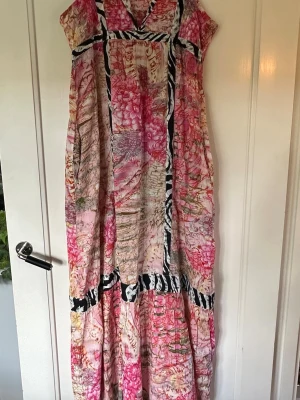 Färgglad långklänning från  S’nob - Säljer en långklänning från S’nob med färgstarkt mönster i rosa, beige och inslag av svartvitt zebramönster. Klänningen är ärmlös, har v-ringning och är tillverkad i ett lätt material som passar perfekt till sommaren. Dragkedja i sidan och hellång på mig (168 cm).