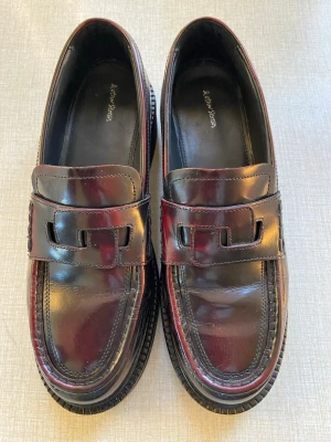 Vinröda loafers från & Other Stories - Snygga vinröda loafers i blankt konstläder från & Other Stories. Klassisk penny loafer-design med markerad sula och stilren siluett. Perfekta för dig som vill ha en tidlös och trendig look.