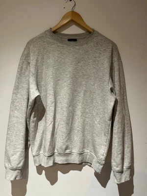HM sweatshirt - En stilren ljusgrå sweatshirt med rund hals och långa ärmar. Tröjan har en avslappnad passform och ribbade muddar vid ärmslut och nederkant. Perfekt för en enkel och clean look. Materialet känns mjukt och bekvämt mot huden.