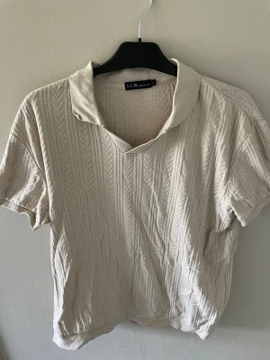 Beige stickad pikétröja från S.C.W - Snygg beige stickad pikétröja från S.C.W med korta ärmar och klassisk krage. Tröjan har ett diskret mönster i stickningen som ger en stilren look. Perfekt för dig som gillar en avslappnad men trendig stil.