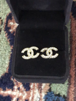 CC guld örhängen med strass - Snygga C örhängen i klassisk CC-logga, täckta med glittrande strass. Örhängena är guldiga och kommer i en svart ask. Perfekta för dig som vill ha en lyxig och trendig accessoar.