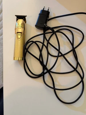 Guld trimmer BabylissPRO - Snygg och stilren trimmer från BabylissPRO i guldigt metallmaterial. Perfekt för att fixa detaljer och linjer i håret eller skägget. Kommer med laddare och har ett greppvänligt handtag. Enkel att använda och ger ett proffsigt resultat.