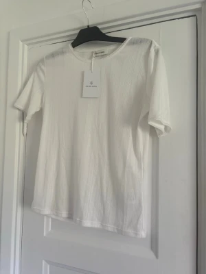 Vit ribbad t-shirt från Anine Bing - Säljer en stilren vit t-shirt från Anine Bing. T-shirten har ribbad struktur, rund halsringning och korta ärmar. Perfekt basplagg som funkar till allt och är tillverkad i mjuk bomull för maximal komfort. Nypris 2600:- storlek Medium. Köpt på NK. Prislapp kvar. Oanvänd. Slutsåld. 