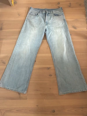 Ljusblåa vida jeans - Säljer ett par ljusblåa jeans med breda ben och klassisk femficksdesign. Jeansen har hög midja och en avslappnad passform, perfekta för en trendig och bekväm stil. Materialet är denim i bomull.