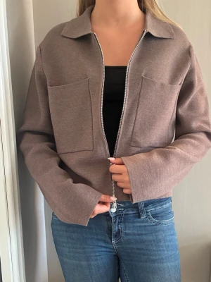Brun ziptröja med fickor från Åhléns - Säljer en brun ziptröja/cardigan  med två stora fickor framtill. Tröjan har krage, långa ärmar och är tillverkad i ett mjukt stickat material. 350kr+ frakt, priset går att diskuteras