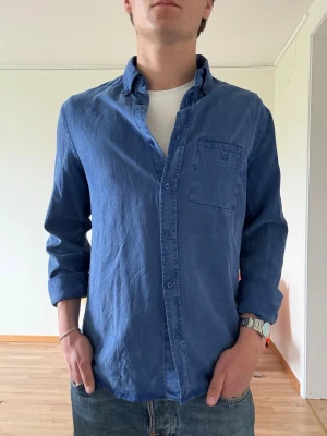 Blå skjorta i tencel - Snygg blå skjorta i tencel med klassisk krage och bröstficka. Skjortan har långa ärmar och knäppning framtill. Perfekt för en avslappnad men stilren look.