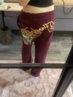 Vinröda Ed Hardy mjukisbyxor  - Säljer ett par vinröda Lågmidjade mjukisbyxor från Ed Hardy med ikoniskt tigertryck och gul text på baksidan.  Perfekta för dig som gillar streetwear och vill sticka ut med cool design. Priset går att diskutera vid snabb affär💗