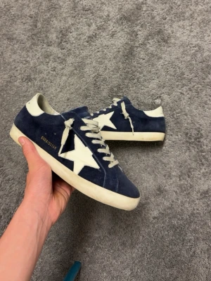Golden Goose blåa sneakers med stjärna - Snygga blåa sneakers från Golden Goose med vit stjärndetalj på sidan och vit häl. Skorna har mockaöverdel, vita skosnören och en klassisk låg siluett. Perfekta för dig som gillar streetstyle och vill sticka ut med en ikonisk design.