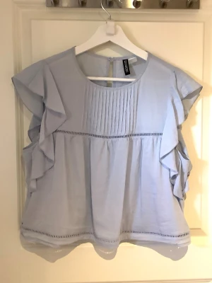 Ljusblå volangblus från H&M - Ljusblå blus med volangdetaljer längs ärmarna.  Jätte fin blus perfekt till sommarn 🩷🩷älskar denna blus men måste tyvärr sälja den pga att den är för kort för mig i år, köpt förra sommarn men knappt använd 💗Går ej att köpa i butik längre tyvärr💕