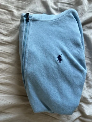 Ljusblå hoodie från Polo Ralph Lauren - Snygg ljusblå hoodie med dragkedja från Polo Ralph Lauren. Klassisk design med huva och dragsnören, två fickor framtill och broderad logga på bröstet. Mjuk bomullskänsla som är perfekt för chill dagar.