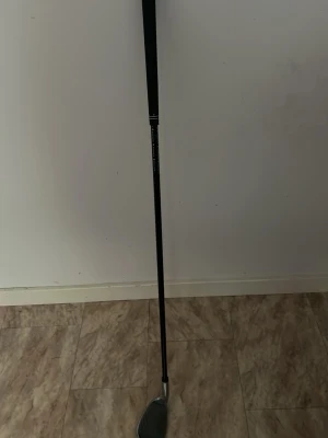 Svart och silver golfklubba junior (sand wedge) - Golfklubba med svart skaft och silverfärgat klubbhuvud. Perfekt för dig som vill förbättra ditt spel på golfbanan. Klubbhuvudet har tydliga räfflor för bra bollkontakt. Materialet är metall och greppet är i svart gummi.