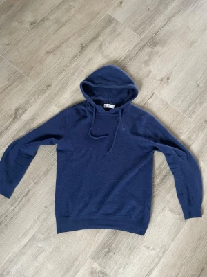 Mörkblå hoodie från Bivaldi - Mysig mörkblå hoodie från Bivaldi med broderad logga på bröstet. Klassisk modell med huva och dragsko, tillverkad i mjukt material som passar perfekt för chill dagar. Långärmad och enkel design som funkar till det mesta.