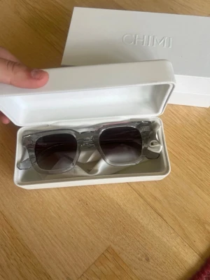 Transparenta solglasögon från CHIMI - Snygga solglasögon från CHIMI med transparent, fyrkantig båge och mörka glas. Kommer i original vit hård ask med CHIMI-logga. Perfekta för dig som vill ha en clean och modern look i sommar.