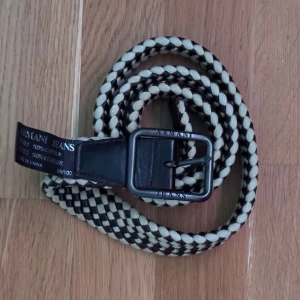 Armani Bälte - Snyggt flätat bälte från Armani Jeans med ett brunt och beige rutigt mönster. Tillverkat i 100% bomull med läderdetaljer. Perfekt för att ge din outfit en stilfull touch