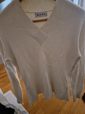 Beige stickad tröja från Wera - Snygg beige stickad tröja från Wera med bred v-ringning och ribbade detaljer. Tröjan har lång ärm och är tillverkad i ett mjukt, tunt stickat material som känns skönt mot huden. Perfekt att matcha med jeans eller kjol. Lite nopprig