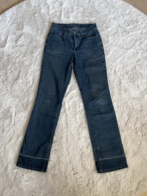 Blå bootcut jeans från Mac - Säljer ett par klassiska blå bootcut jeans från Mac. Jeansen har fem fickor, normalhög midja och raka ben med lätt utsvängning nedtill. Tillverkade i mjukt denimtyg som ger en skön passform. 