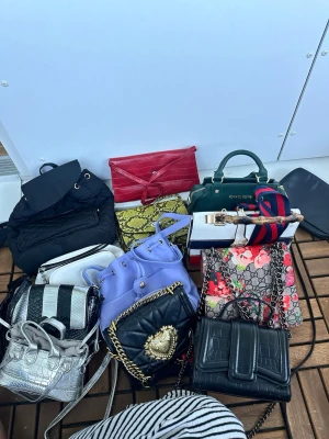 Mix av trendiga handväskor - Säljer ett gäng handväskor i olika färger och material, bland annat svart quiltad väska med guldkedja, röd kuvertväska, grön handväska med handtag, lila bucket bag och mönstrad väska med blommor. Perfekt för dig som vill ha variation i din stil.
